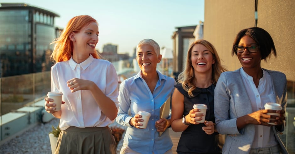 Four business women walking together with coffee cups and smiling