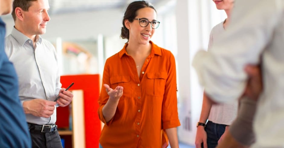 Group of people gathered in a circle with a woman in an orange shirt talking