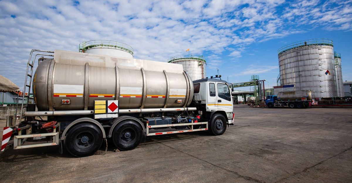 Silver truck in a car park with blue sky and a tank