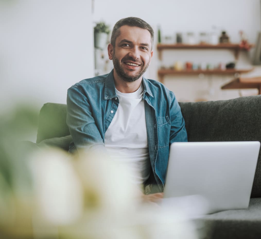 Man sitting on sofa and looking up from his laptop smiling