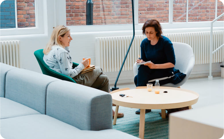 Two woman sitting on chairs with coffee cups and talking