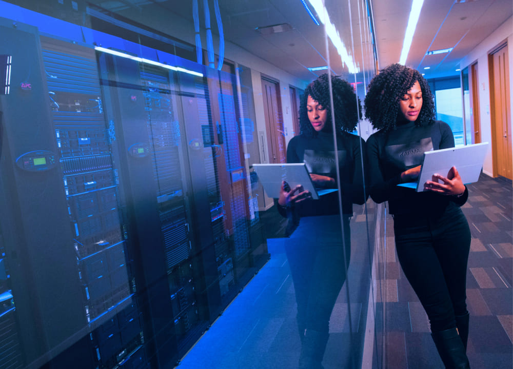 Woman in a corridor with tech servers looking at her laptop